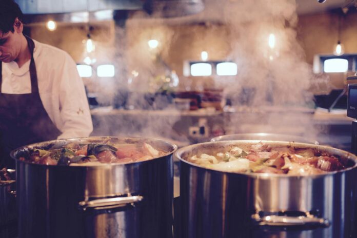 man wearing black apron near two silver metal cooking pot